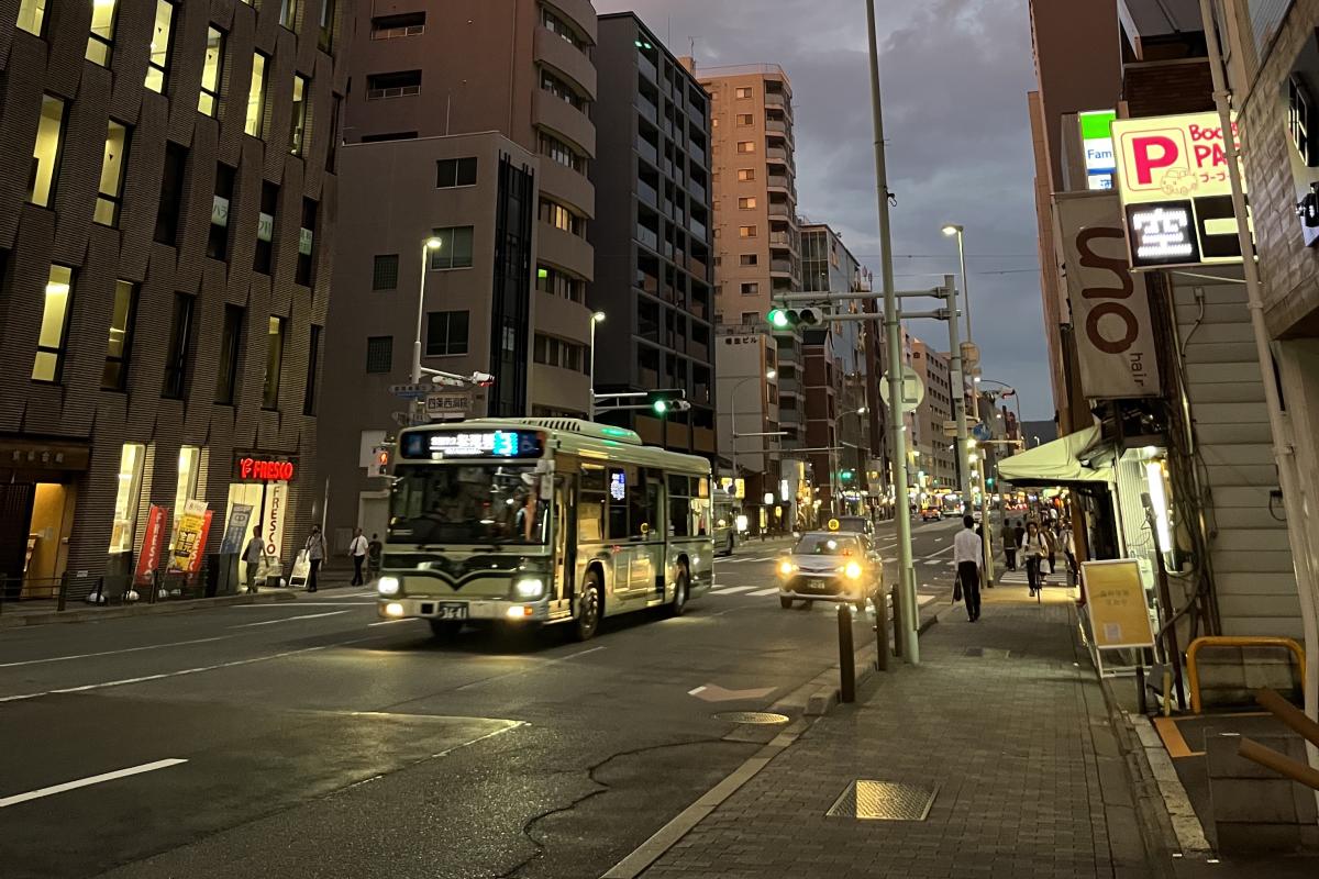 Evening photo of a bus on the street with tall buildings on either side